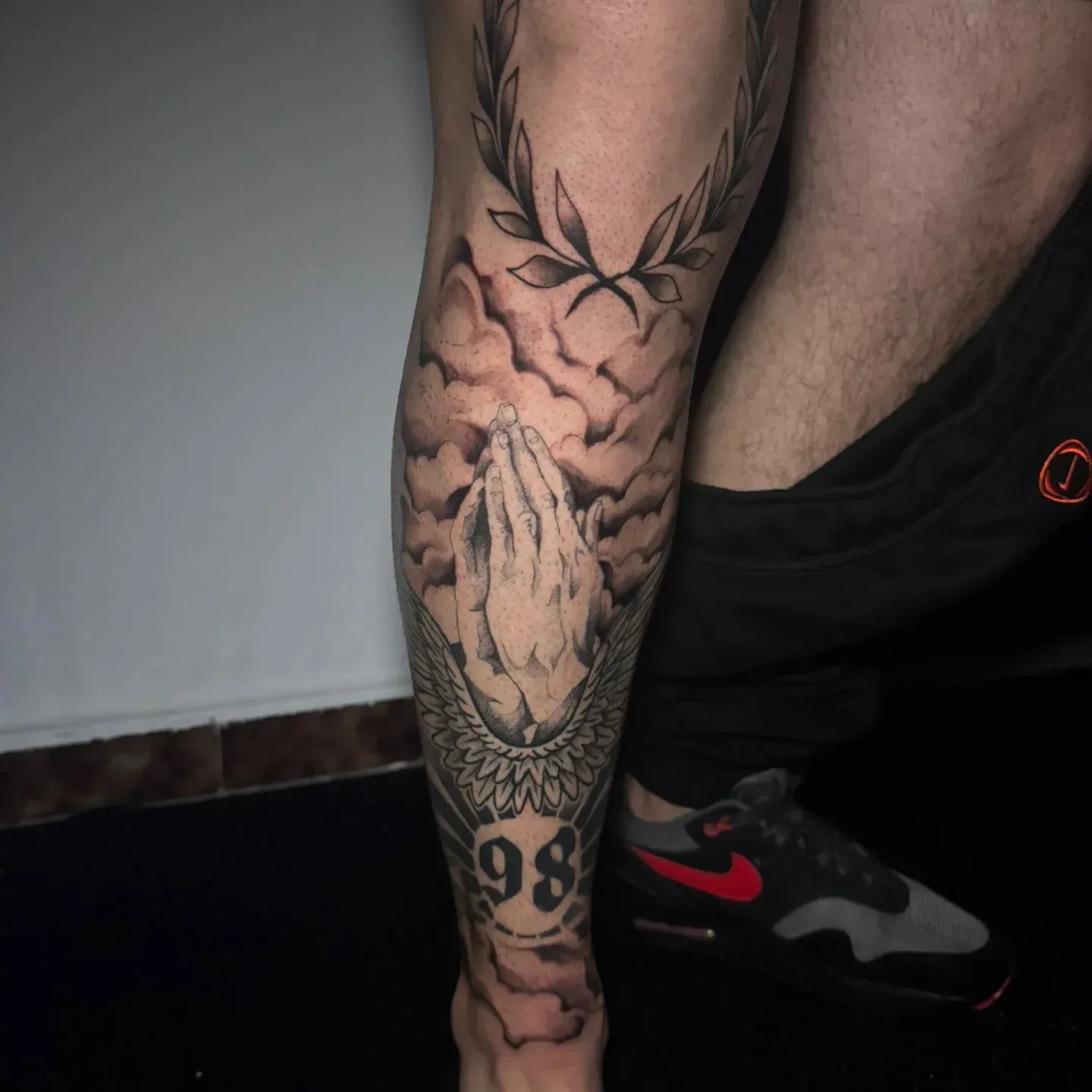 Tatuaje en la pierna de una calavera rugiente con astas y el número «98» cerca del tobillo, junto a un zapato Nike negro