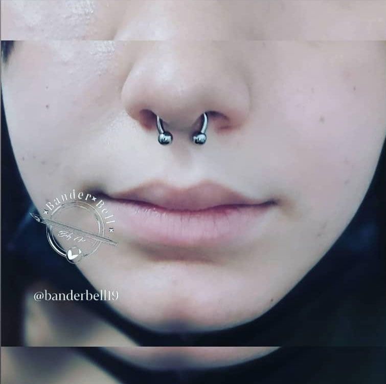Primer plano de un rostro con piercings en ambas fosas nasales y los labios en una expresión neutra.