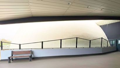 Intérieur d'un bâtiment moderne avec un mur blanc incurvé, une balustrade en verre et un banc.