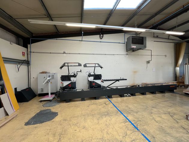 Une grande scie industrielle dans un atelier aux murs blancs et à l'éclairage zénithal.