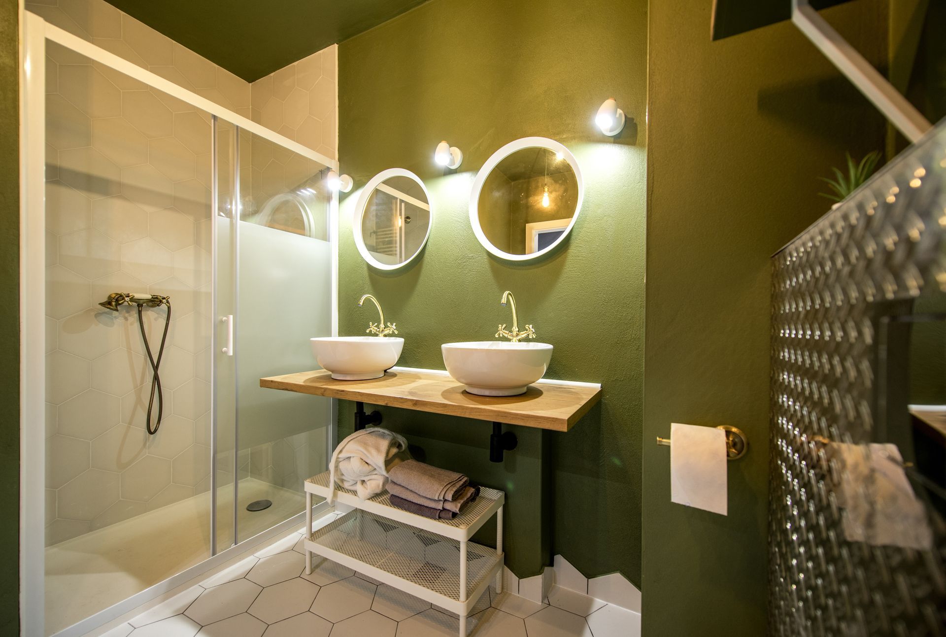 Salle de bains moderne avec douche en verre, murs verts, double vasque et miroirs ronds.