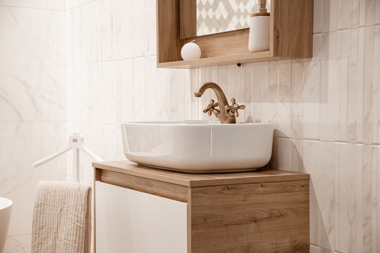 Meuble-lavabo moderne avec vasque blanche, armoire en bois et mur carrelé avec étagère.
