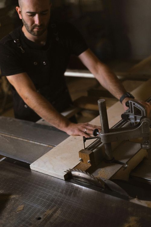 Un homme utilise une scie pour couper une planche dans un atelier sombre.