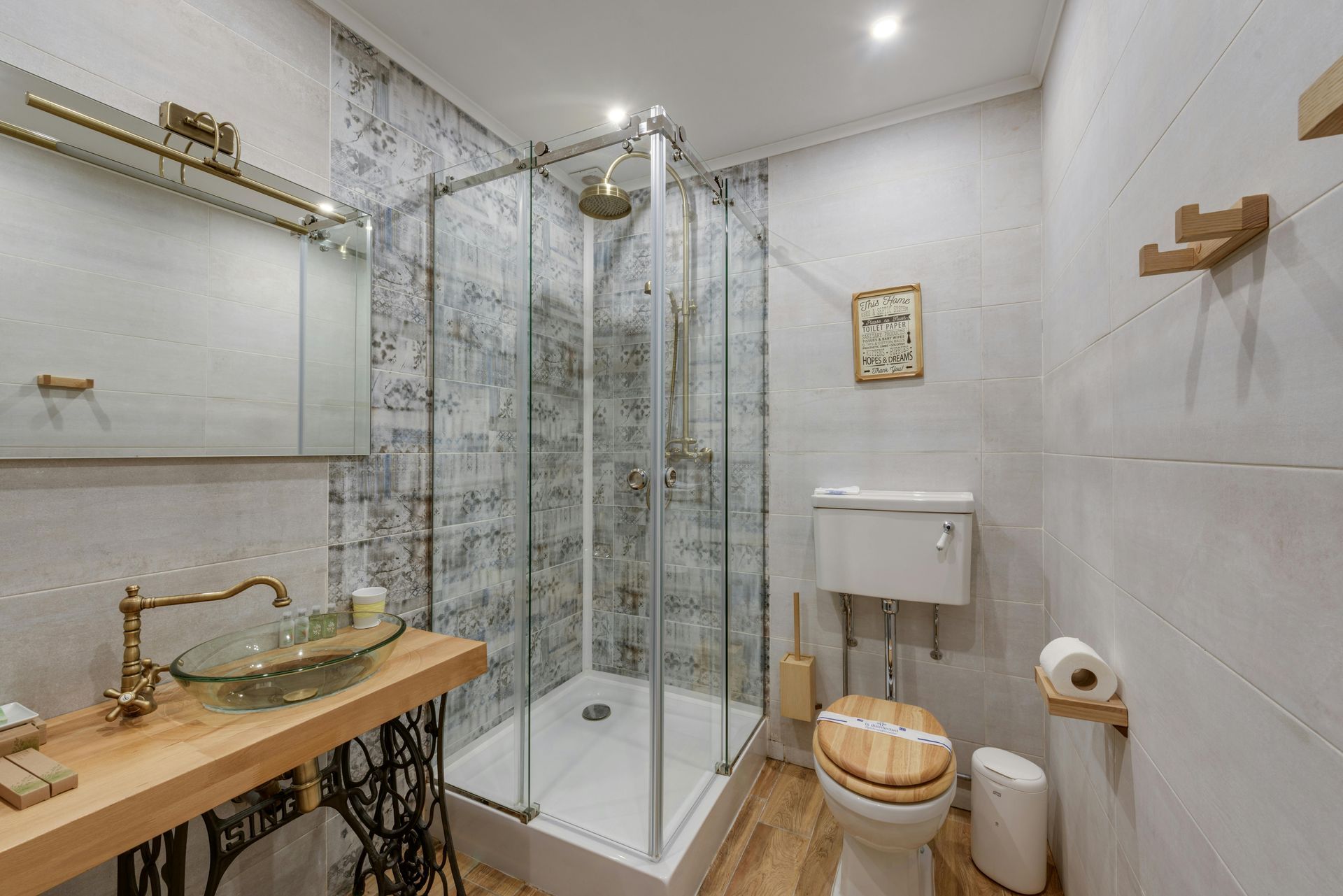Salle de bains élégante avec douche en verre, robinetterie dorée, meuble-lavabo en bois et carrelage en marbre.