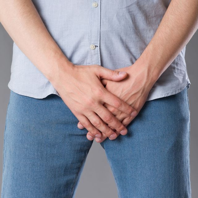 Un hombre con camisa azul y jeans azules tiene las manos en el estómago.