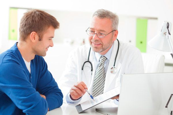 Un médico está hablando con un paciente que está sentado en un escritorio.