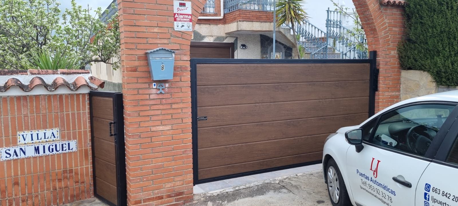 Una puerta corredera marrón y una puerta de entrada lateral, situadas en una pared de ladrillo con la inscripción 