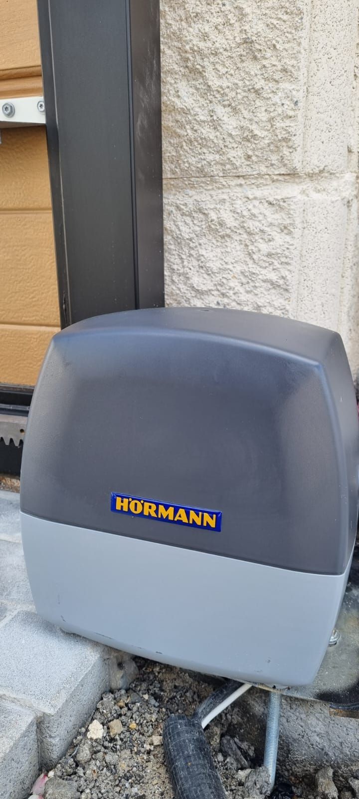 Un motor para puerta corredera Hörmann de color gris y antracita montado sobre una superficie de piedra junto a una puerta.