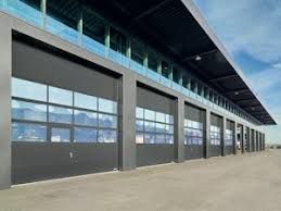 Exterior de un edificio comercial moderno con múltiples puertas de garaje de cristal en una fachada gris oscuro bajo un cielo azul despejado.