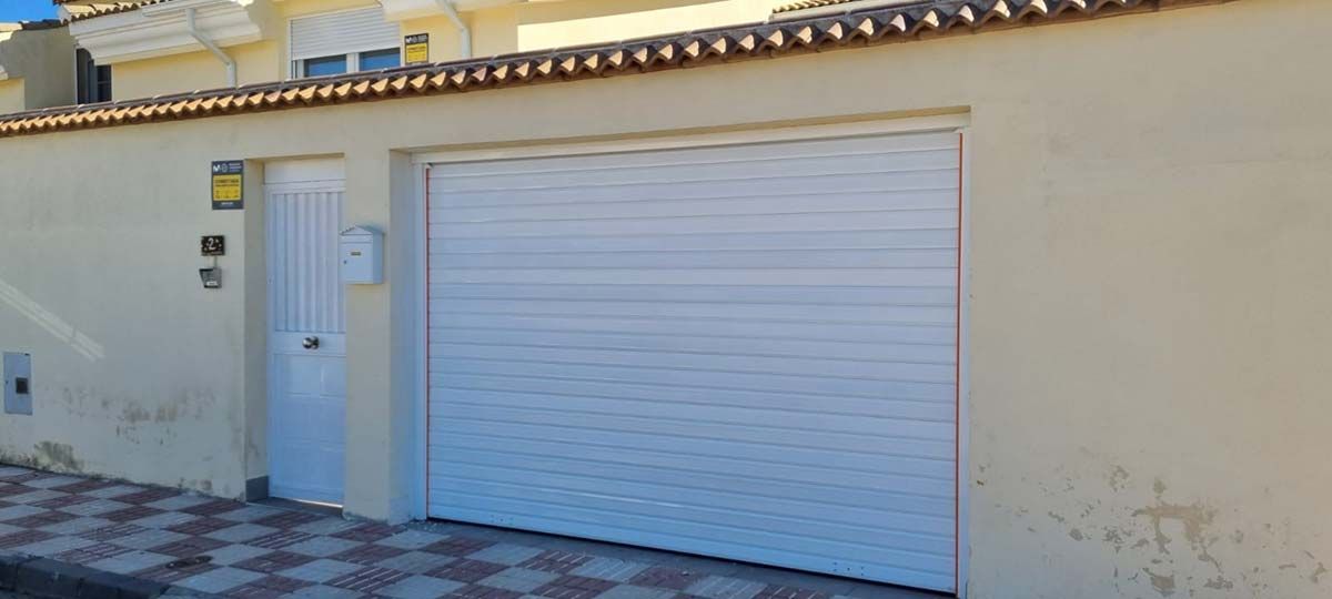 Puerta de garaje blanca y puerta de entrada a juego en un edificio de color amarillo claro con techo de tejas.