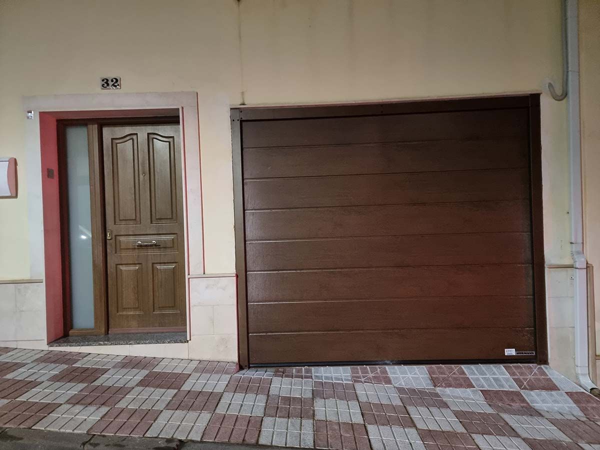 Puerta de garaje marrón y puerta de madera al lado de una casa con una pasarela con diseño de ladrillo.