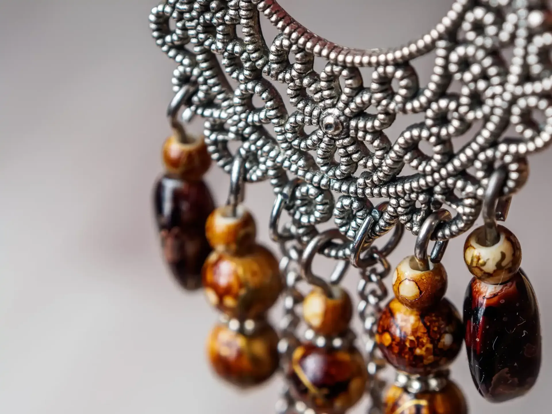 Primer plano de un intrincado pendiente de filigrana plateada con cuentas colgantes de color ámbar jaspeado.