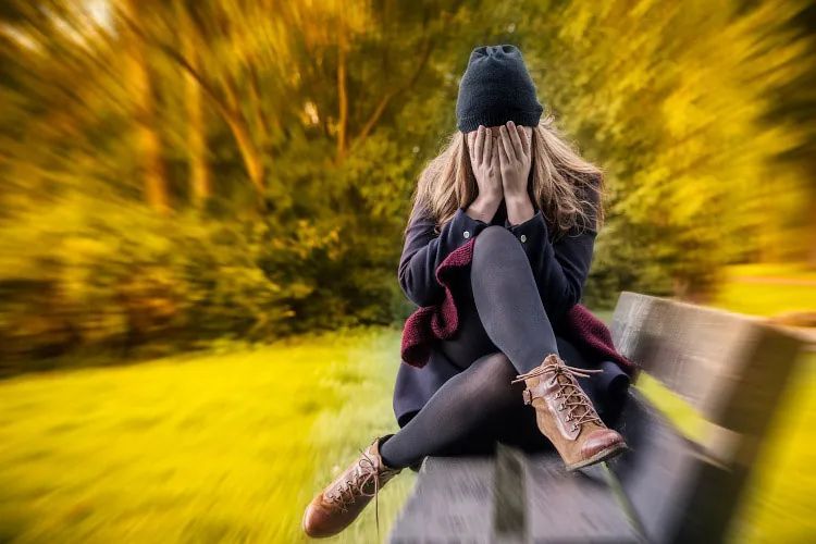 Una mujer está sentada en un banco del parque cubriéndose la cara con las manos.