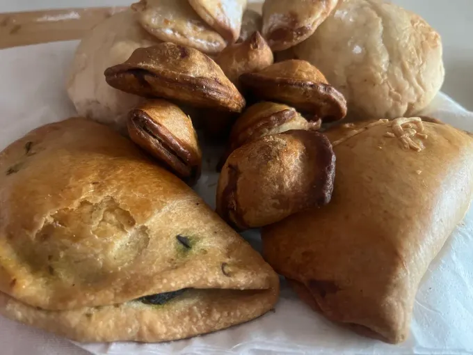 Variedad de pasteles y galletas dispuestos en un plato, incluyendo empanadillas triangulares y pequeños dulces de almendra.
