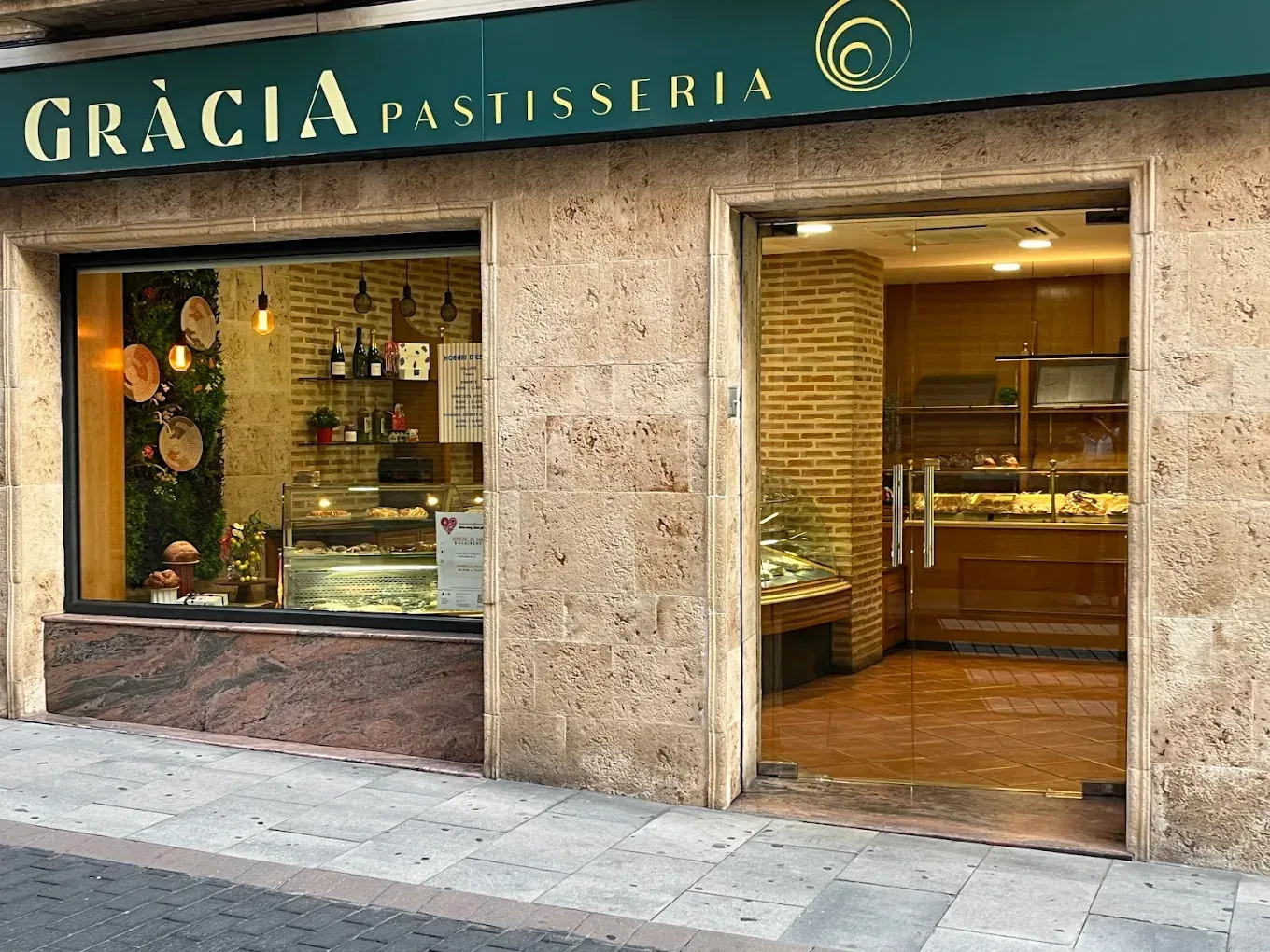 Exterior de la pastelería Gràcia con escaparate y entrada abierta en una calle empedrada.