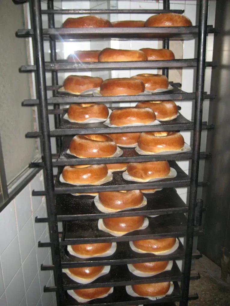 Estantes con bandejas llenas de panes recién horneados en la zona del horno de la panadería.
