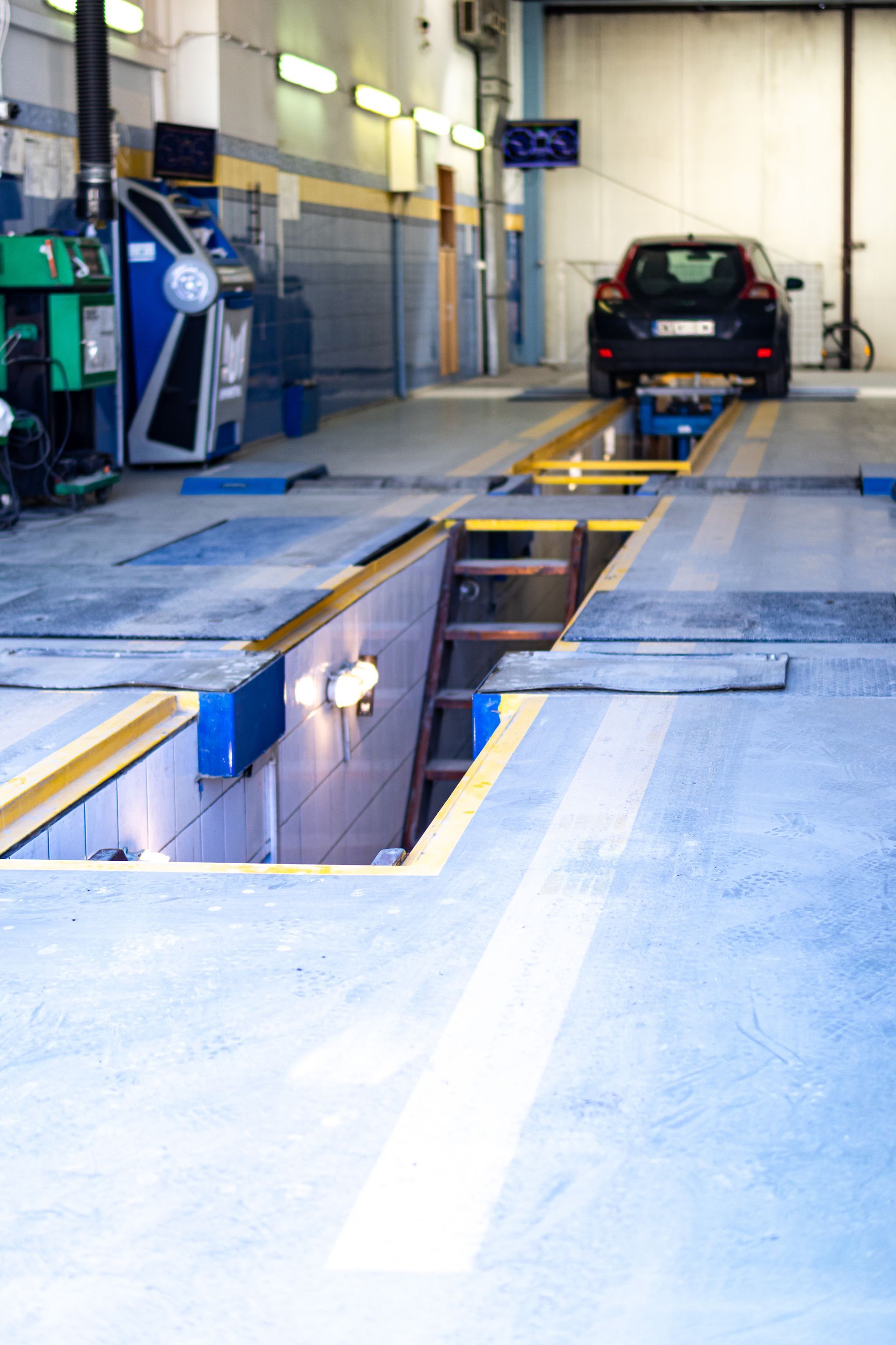 Un poste d'inspection de véhicules avec une fosse de maintenance profonde au premier plan et une voiture positionnée au fond de l'atelier.
