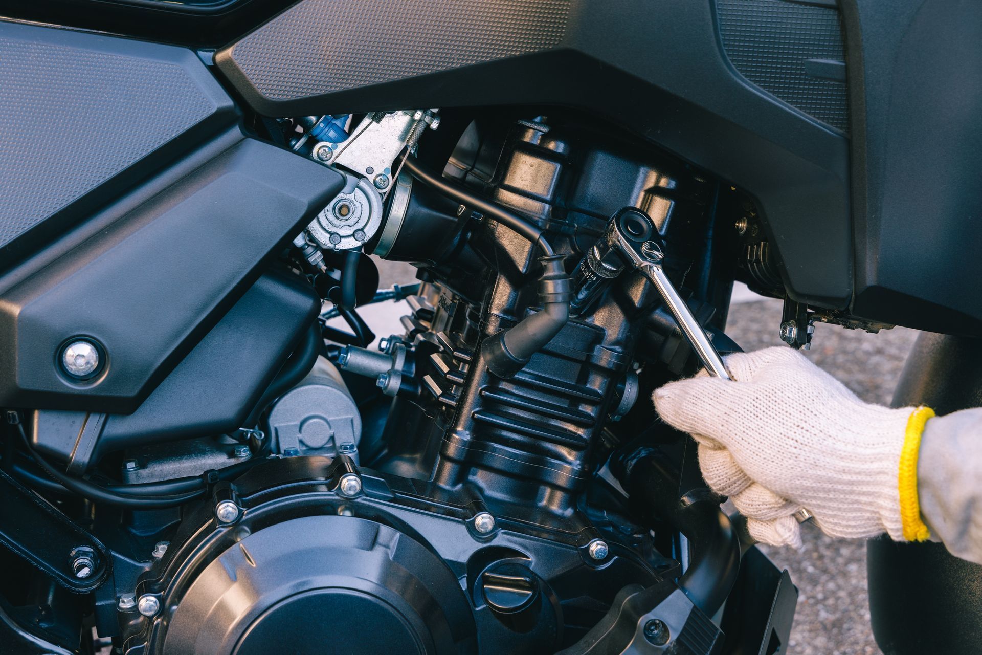Une personne portant un gant blanc utilise une clé à cliquet pour travailler sur le moteur d'une moto.