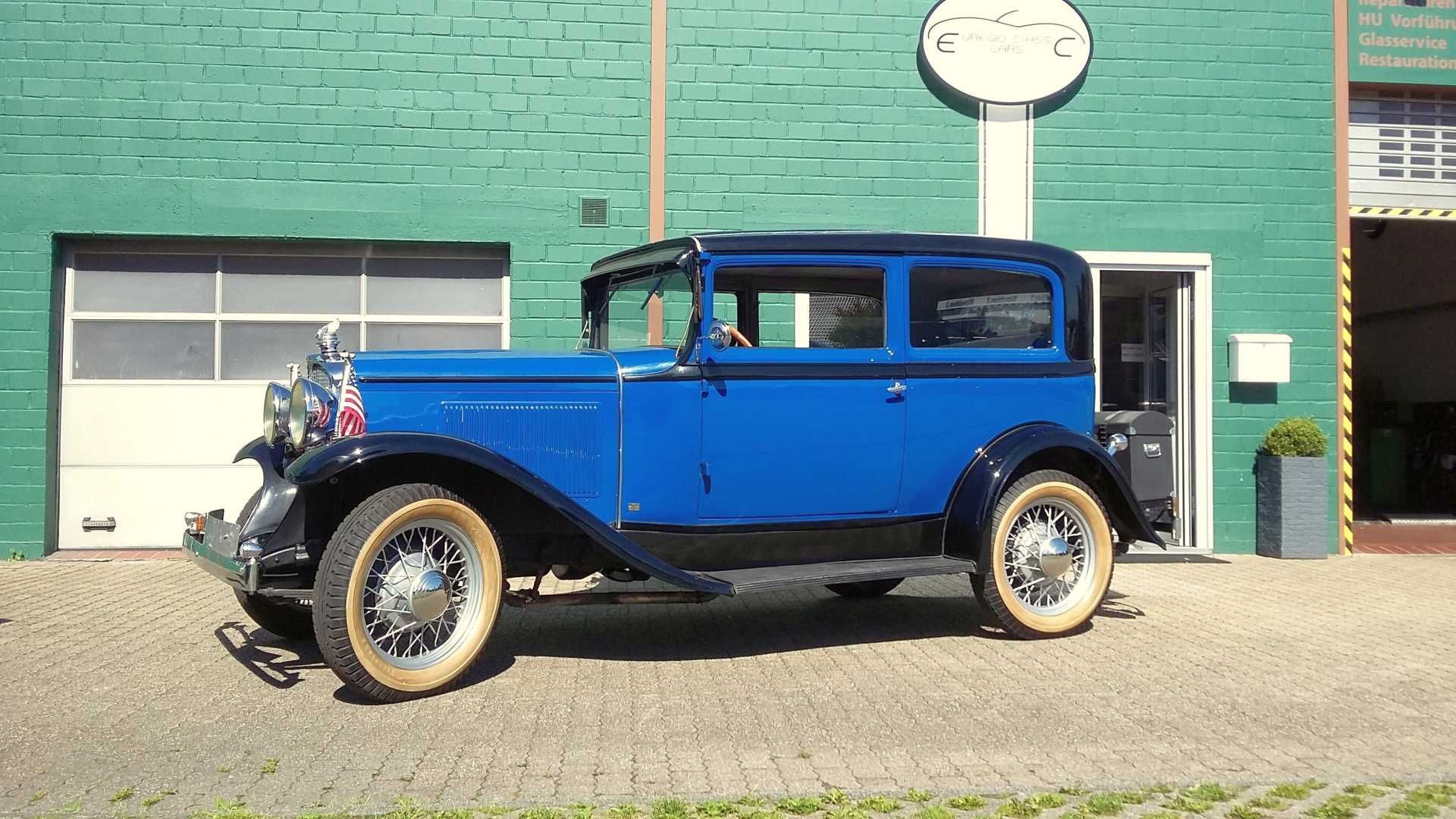 Ein altes blaues Auto steht vor einem grünen Backsteingebäude.