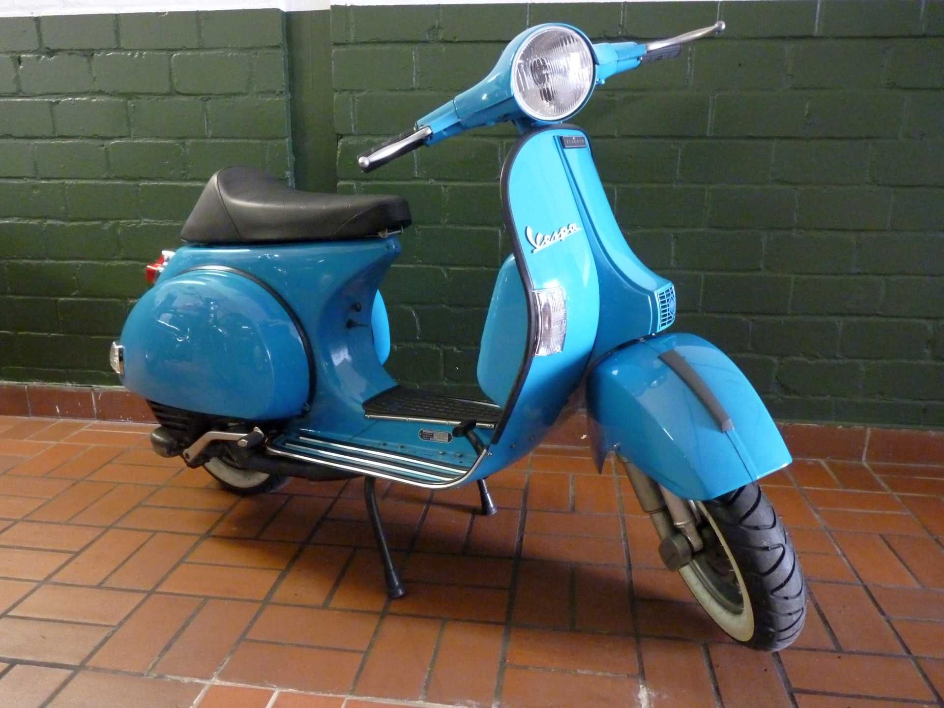 Ein blauer Vespa-Roller steht auf einem gefliesten Boden