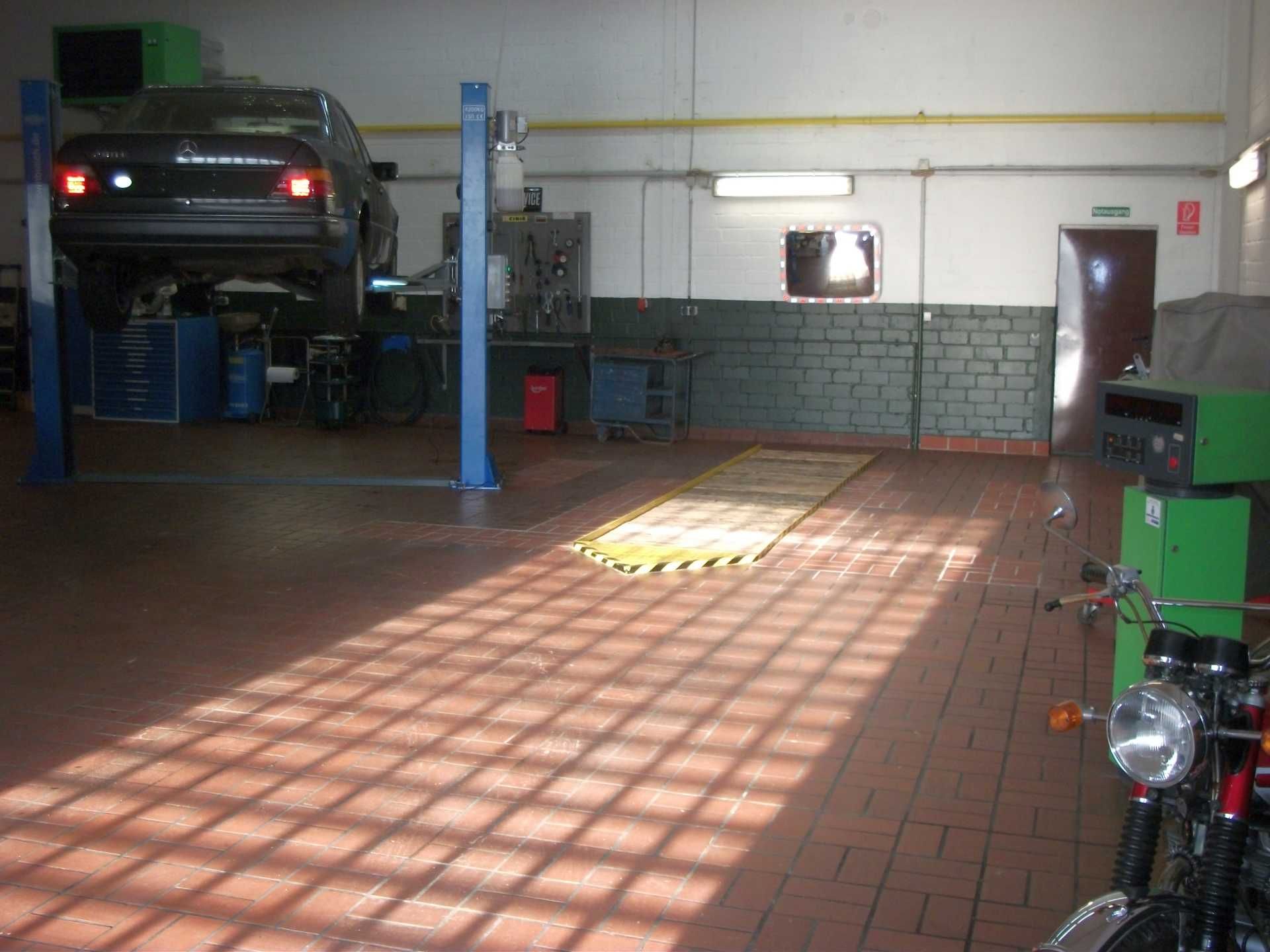 Ein Auto steht auf einer Hebebühne in einer Garage neben einem Motorrad