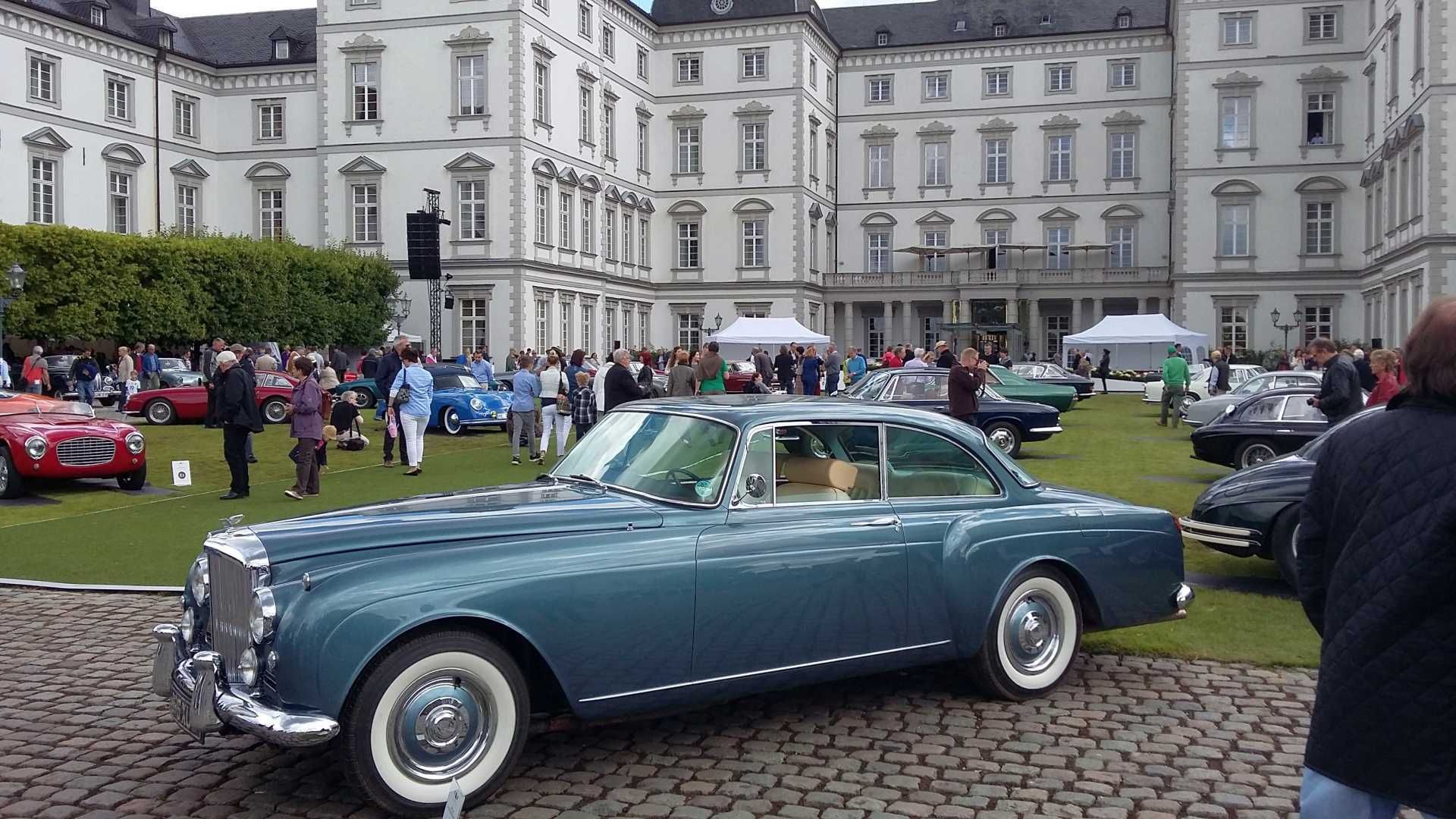 Ein blaues Auto mit weißen Reifen parkt vor einem großen Gebäude.