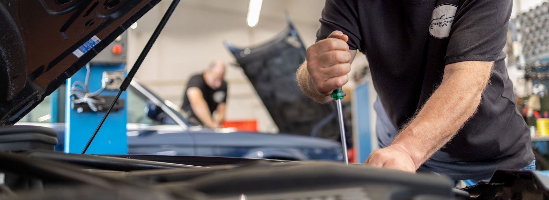 Ein Mechaniker arbeitet in einer Werkstatt unter der Motorhaube eines Autos und benutzt ein Werkzeug in der Nähe des Motors.