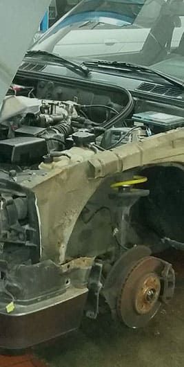 In einer Werkstatt wird an einem Auto mit geöffneter Motorhaube gearbeitet.