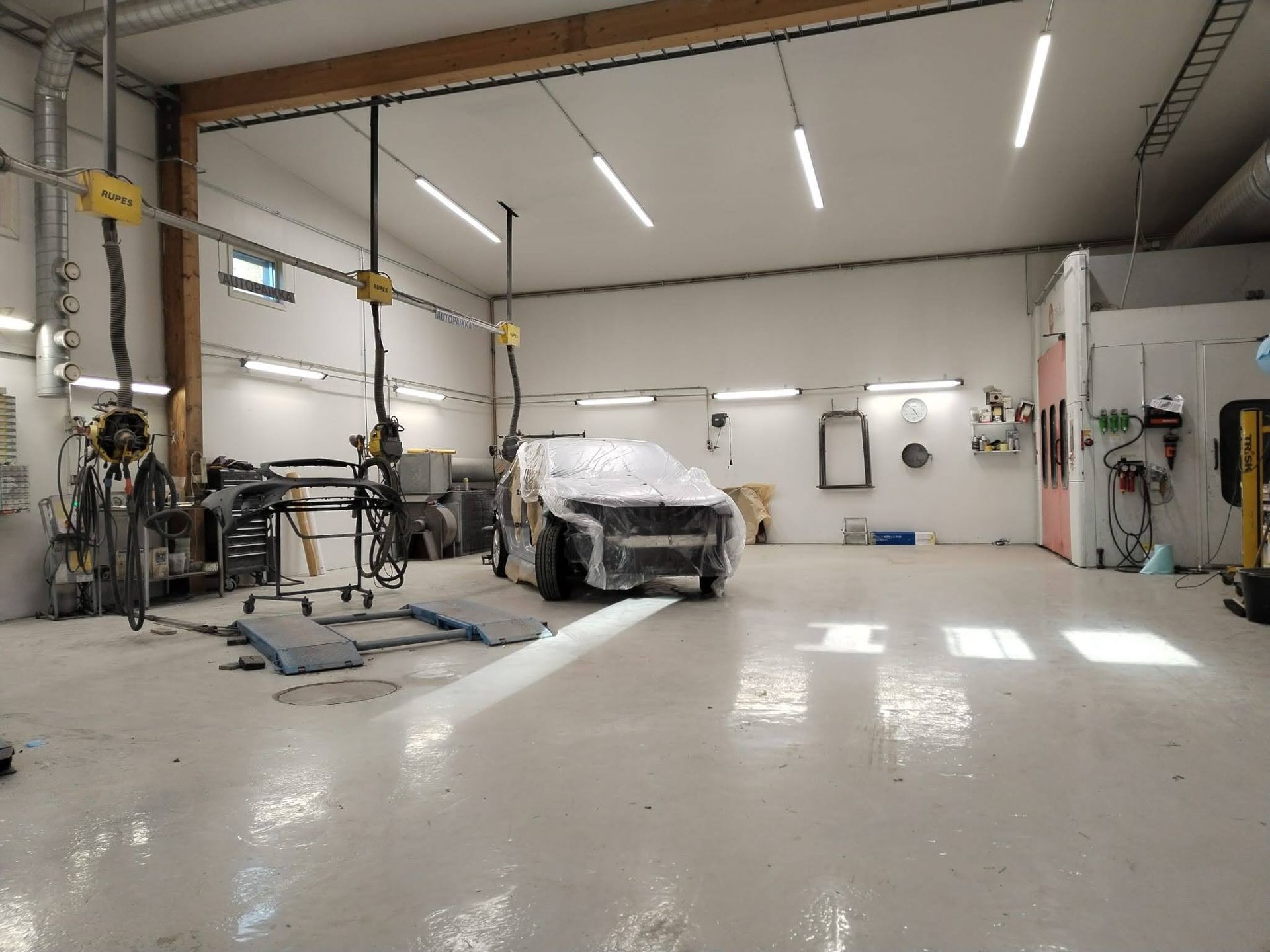 Autokorjaamon sisustus, jossa on katettu auto, nostimet ja kirkkaat kattovalot