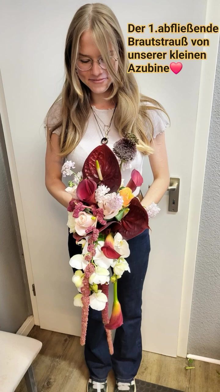 Eine Person hält einen großen, kaskadenförmigen Brautstrauß mit Anthurien, hellen Rosen und hängenden, rosa Blüten.