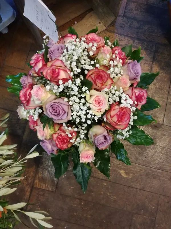 Ein Strauß aus rosa und lavendelfarbenen Rosen, vermischt mit kleinen weißen Füllblumen und grünen Blättern.