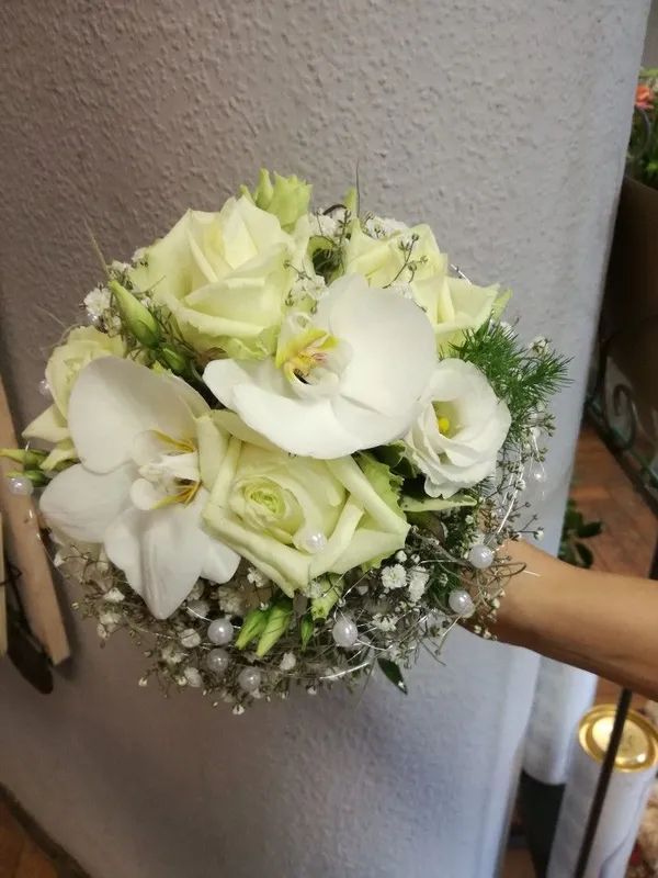 Ein Brautstrauß aus weißen Rosen, Orchideen und Schleierkraut mit kleinen Perlenverzierungen, gehalten von einer Hand.