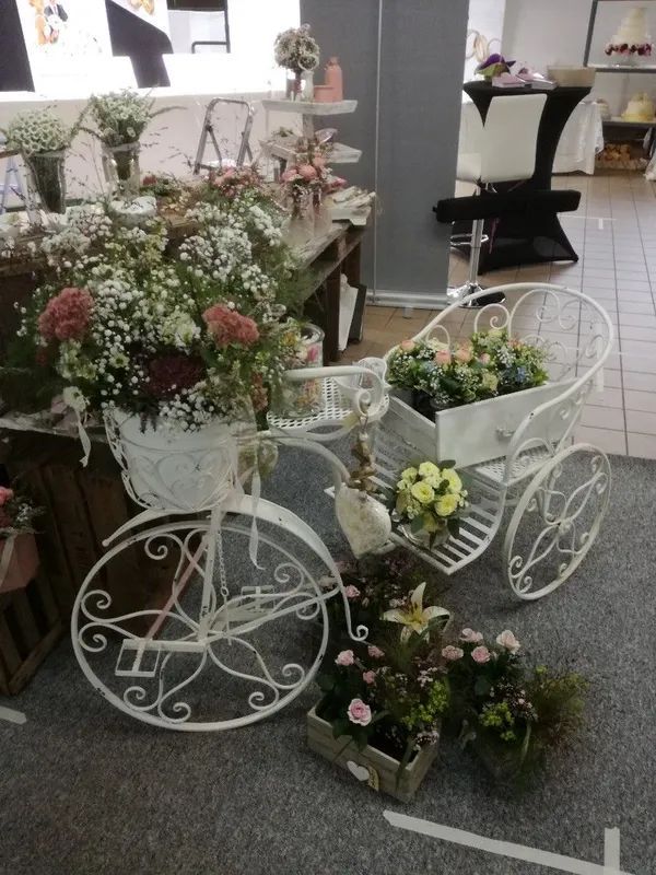 In einem Laden steht ein weißer, dekorativer, dreieckiger Pflanzkasten aus Metall, gefüllt mit Blumen.