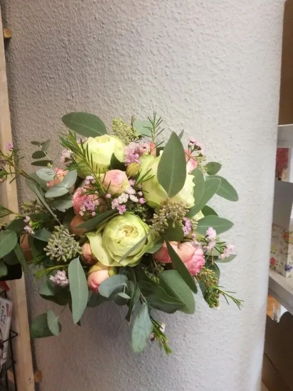 Ein Brautstrauß aus hellgelben Rosen, rosa Sprayrosen und Eukalyptusblättern vor einem schlichten hellgrauen Hintergrund.