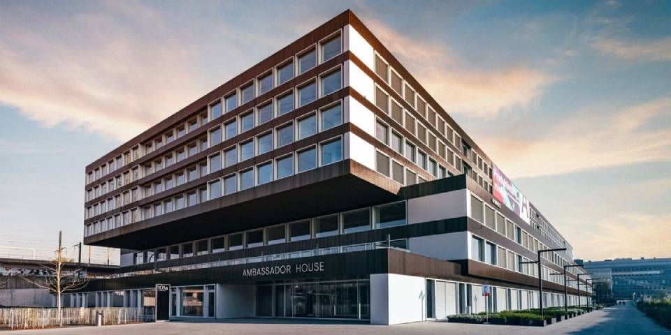 Modernes, mehrstöckiges Bürogebäude mit vielen Fenstern und Flachdach unter einem blau-orangenen Himmel.