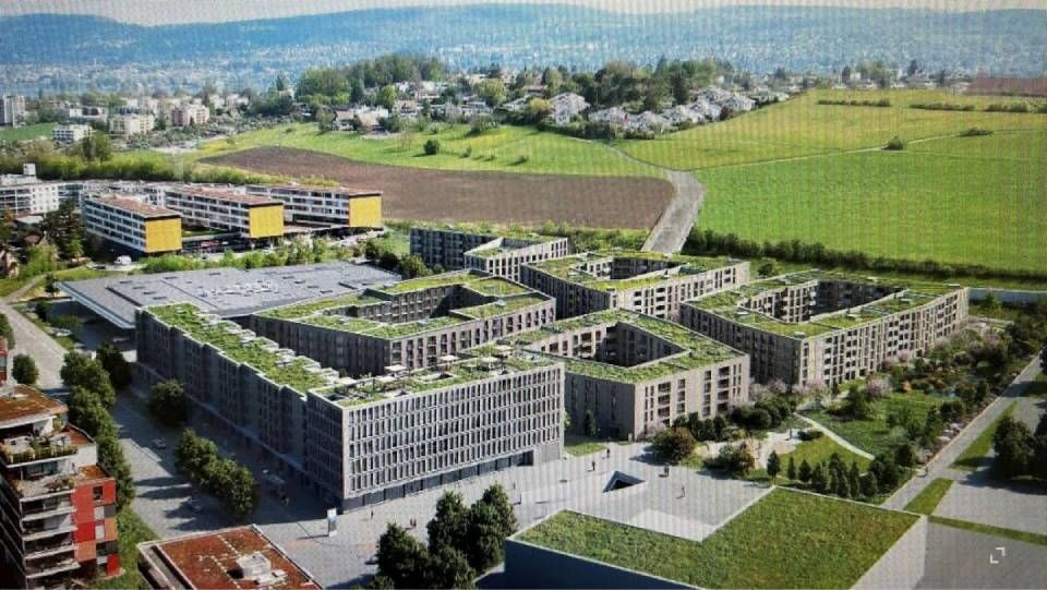 Luftaufnahme moderner Gebäude mit Gründächern in einer grasbewachsenen Umgebung mit Hügeln in der Ferne.