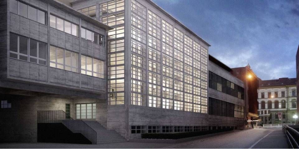 Modernes Betongebäude mit vielen in der Dämmerung erleuchteten Fenstern.