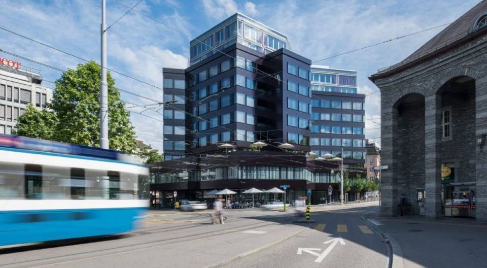 Ein modernes schwarzes Gebäude, neben dem eine blaue Strassenbahn durch eine Stadtstrasse fährt.