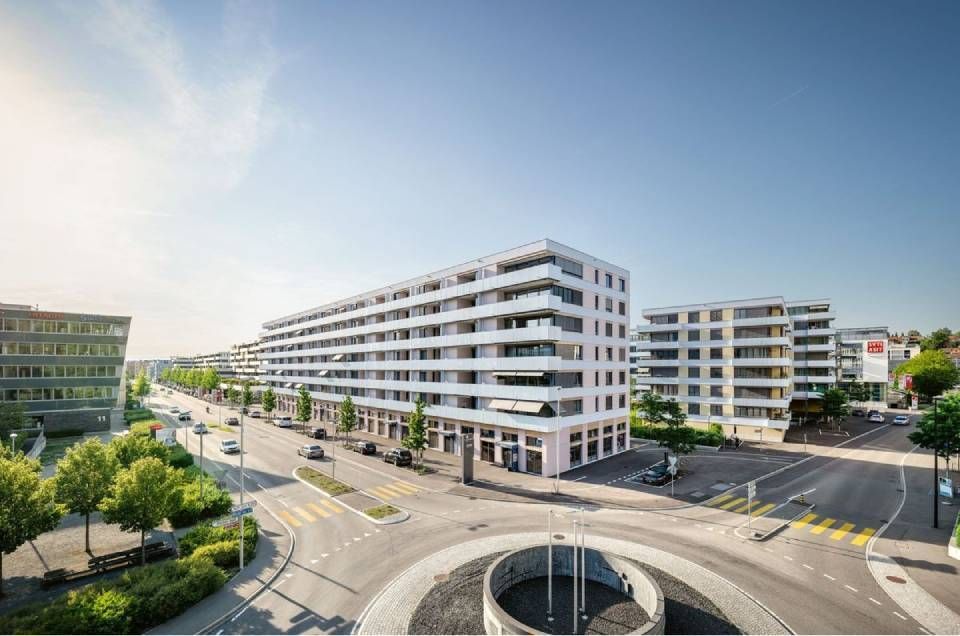 Mehrstöckige weisse Gebäude mit Balkonen in der Nähe eines Kreisverkehrs an einem sonnigen Tag.