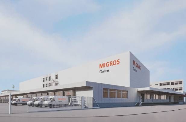 Das Lager von Migros Online mit weissen Lieferwagen unter bewölktem Himmel.