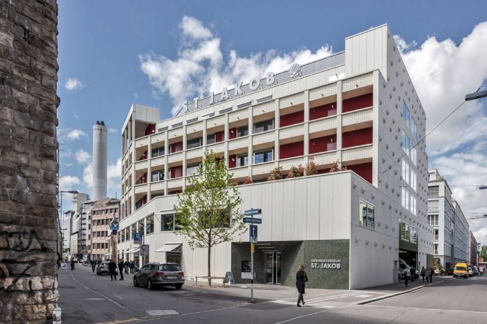 Modernes Gebäude mit weisser Fassade und roten Balkonen an einer Stadtstrasse.