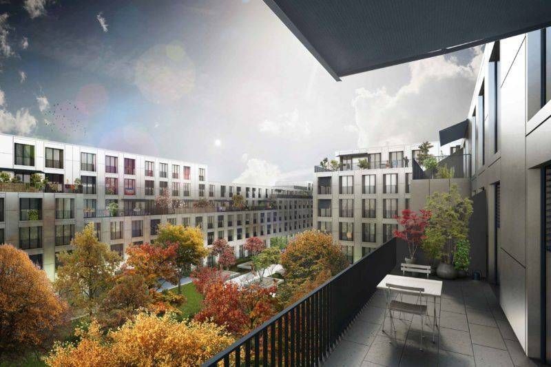 Blick vom Balkon auf moderne Gebäude, die einen grünen Innenhof mit Bäumen im Herbst umgeben.