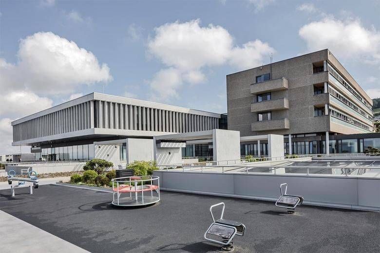 Modernes Krankenhausgebäude mit flachem Dachspielbereich, sonniger Tag.