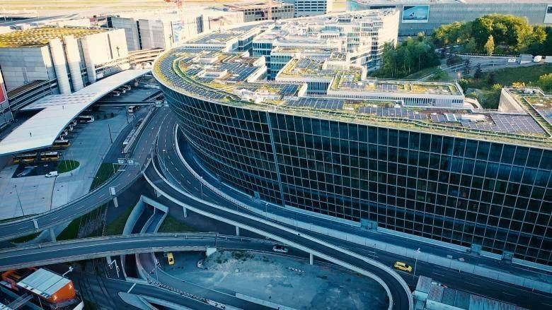 Modernes Glasgebäude mit geschwungenem Gründach, in unmittelbarer Nähe von Strassen und anderen Bauwerken.