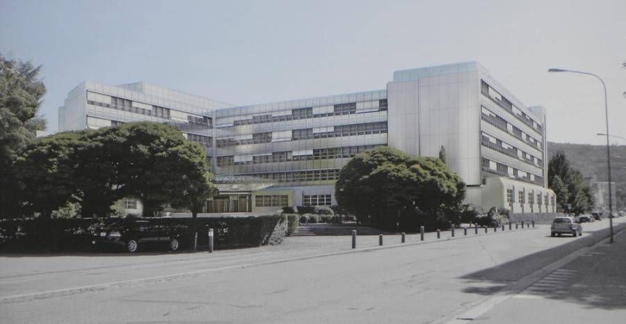 Modernes, mehrstöckiges Gebäude mit heller Fassade, vermutlich ein Krankenhaus. Strasse und Bäume im Vordergrund.