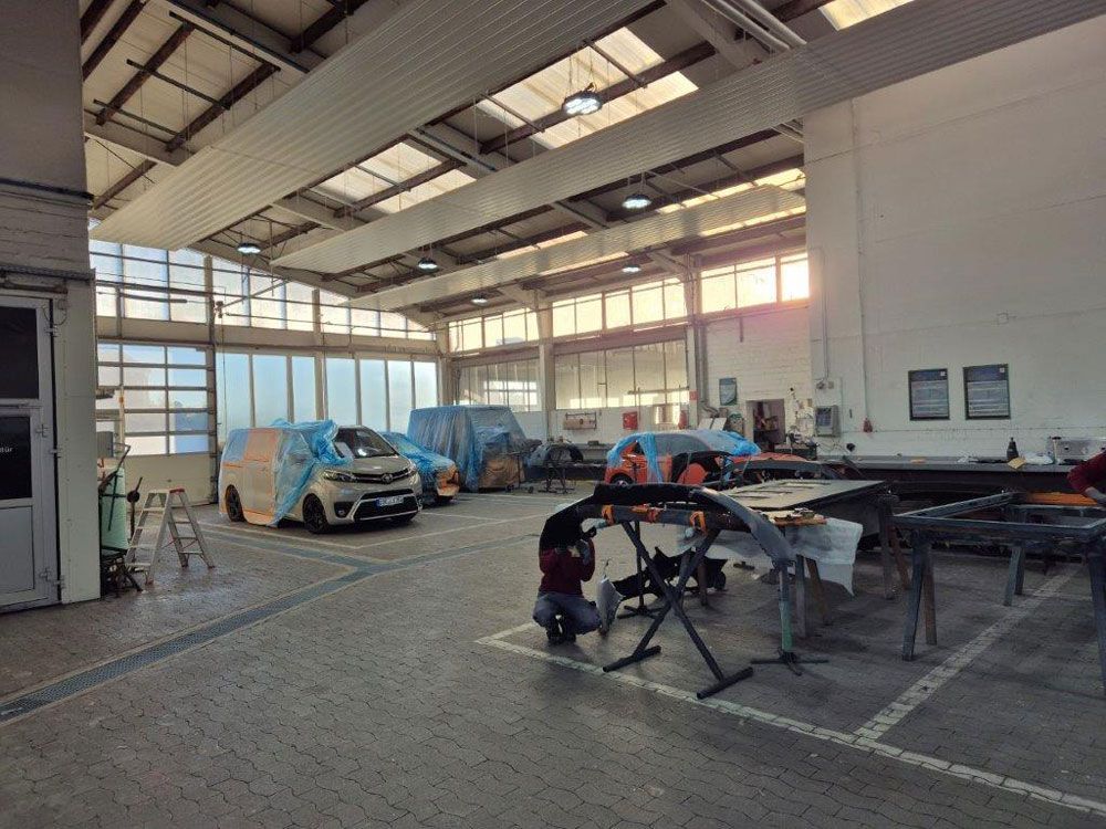 In einer Autowerkstatt: Autos mit blauer Plastikfolie abgedeckt, Arbeiter lackieren, Reparaturarbeiten sind im Gange.