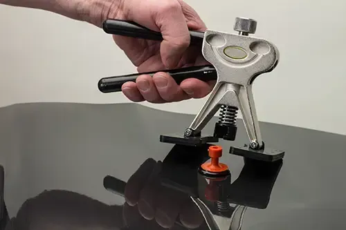 Eine Hand benutzt ein Ausbeulwerkzeug, um eine Delle aus einer schwarzen, glänzenden Oberfläche zu entfernen.