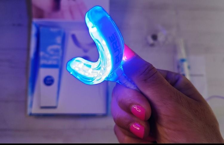 Una persona con uñas rosadas sostiene un dispositivo blanqueador de dientes.