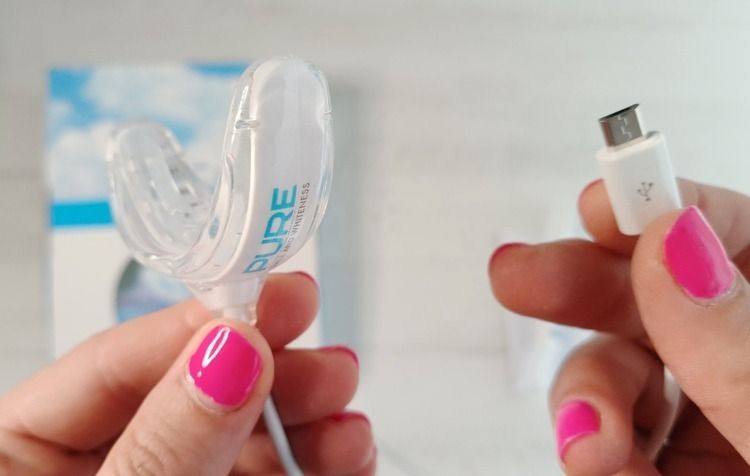 Una mujer sostiene un dispositivo para blanquear los dientes y un cable de carga.