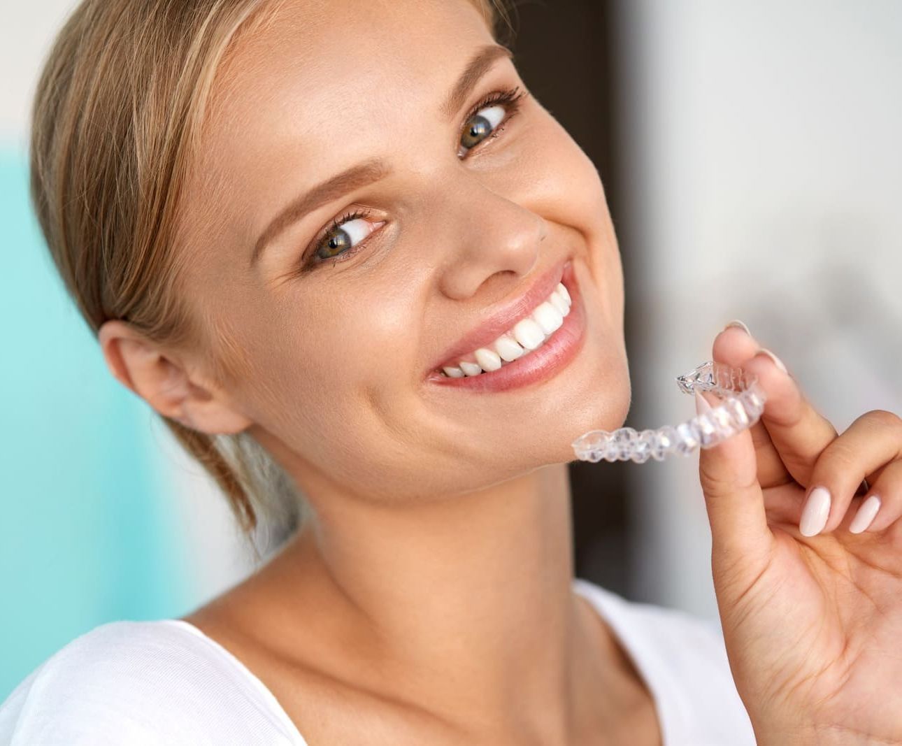 Una mujer sonríe mientras sostiene un aparato transparente en sus dientes.